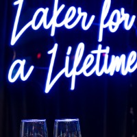 Two Laker for a Lifetime customer champagne flutes on table side my side with Laker for a Lifetime neon sign in background.